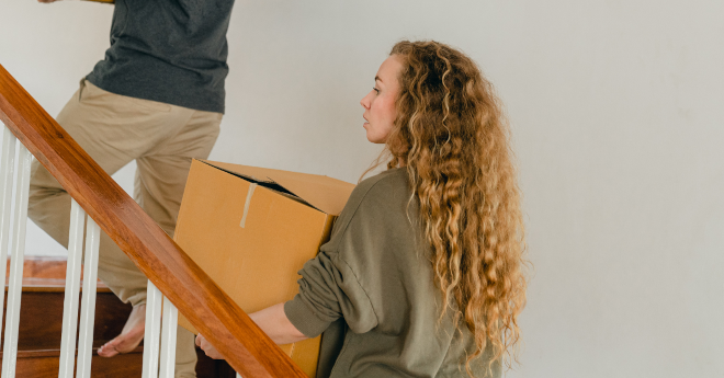 zwei junge frauen tragen umzugaskarton ein treppenhaus hoch